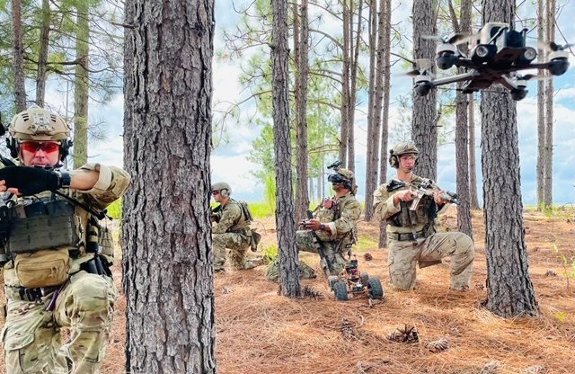 A team in a pine forest working with a quadcopter overhead and a ground robot